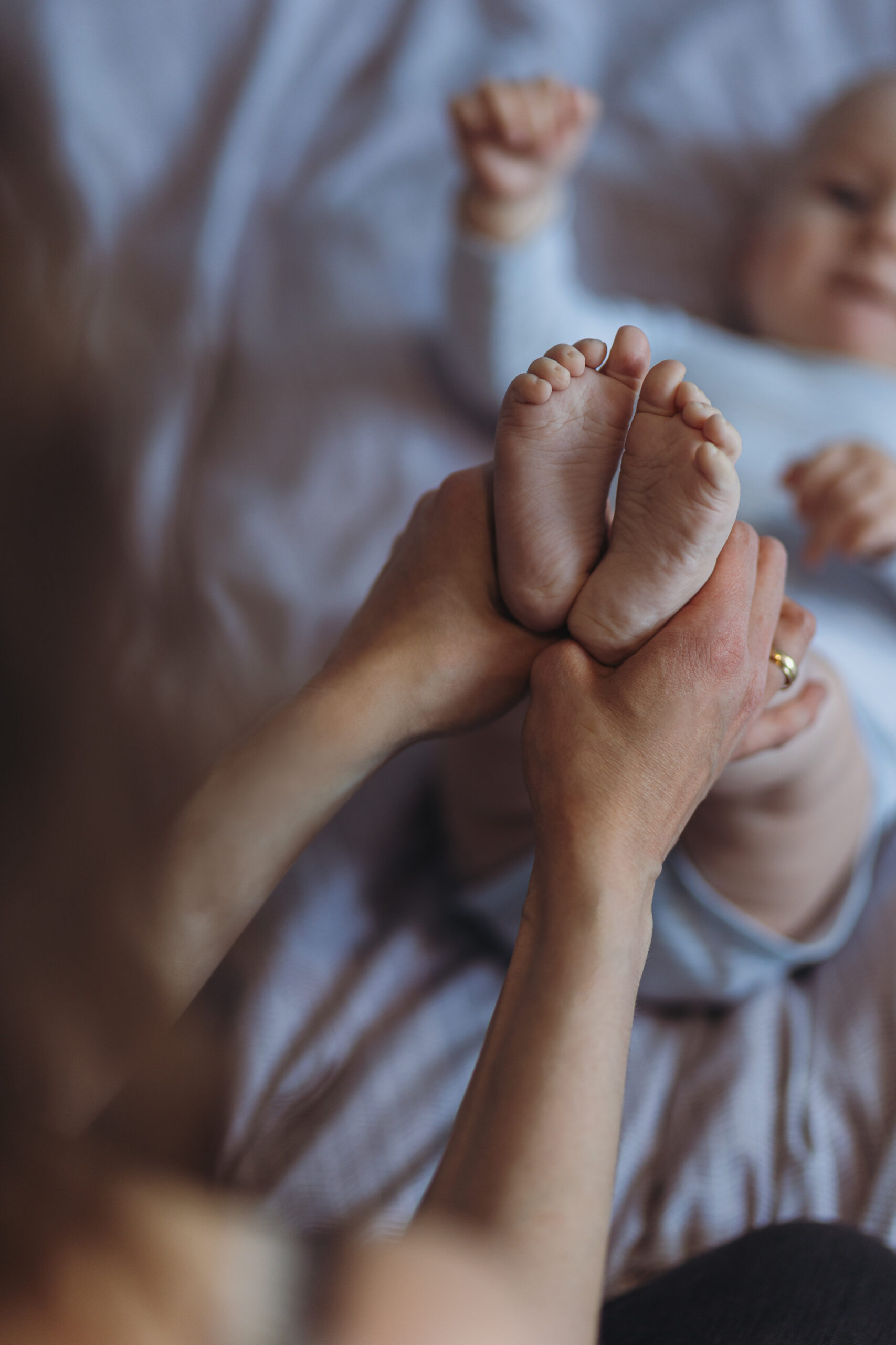 Mama trzymająca stópki niemowlęcia na łóżku podczas domowej sesji rodzinnej w Poznaniu