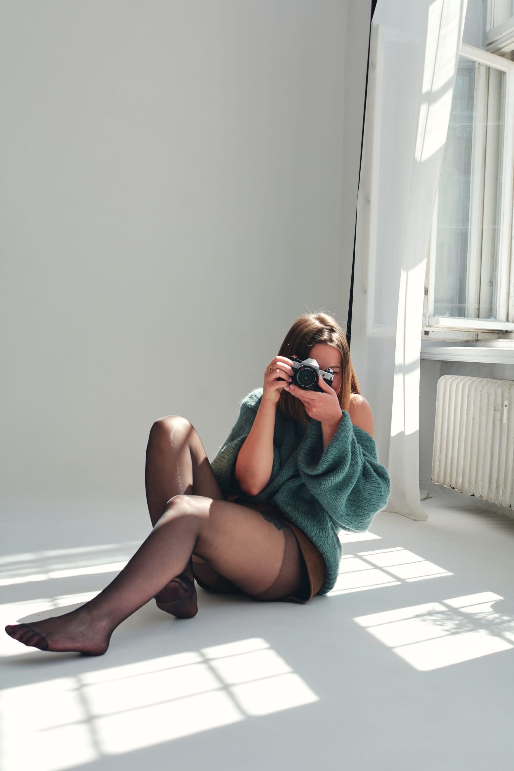 Fotografka siedząca na podłodze i robiąca zdjęcie aparatem podczas sesji w jasnym studio w Poznaniu